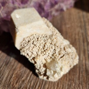 May include: A white crystal cluster with a rough, textured surface. The crystal has a pointed shape and is surrounded by smaller crystals.