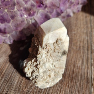 May include: A cluster of white crystals with a large, clear crystal in the center. The crystals are on a wooden surface.