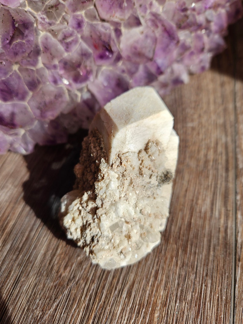May include: A cluster of white crystals with a large, clear crystal in the center. The crystals are on a wooden surface.