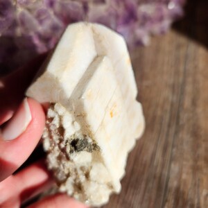 May include: A white, crystalline mineral with a rough, textured surface. The mineral has a layered, stacked appearance, with multiple facets.