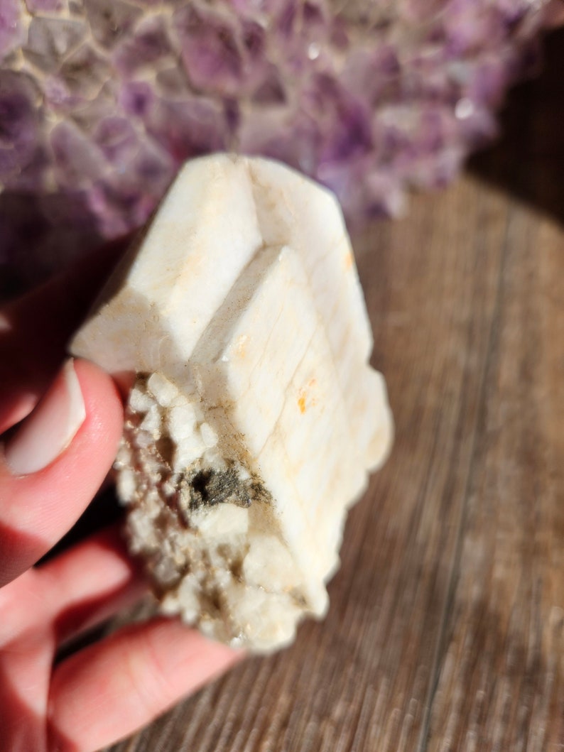 May include: A white, crystalline mineral with a rough, textured surface. The mineral has a layered, stacked appearance, with multiple facets.