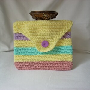 May include: A crocheted yellow, pink, and teal striped clutch with a purple button.