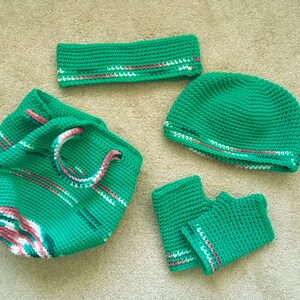 May include: A set of crocheted green accessories with white and pink stripes. The set includes a bag, a hat, a headband, and a pair of fingerless gloves.