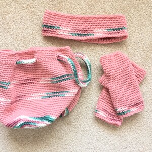 May include: A set of three crocheted items in pink with white and green stripes. The set includes a bucket bag, a headband, and a pair of fingerless gloves.