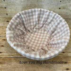 May include: A round, fabric basket with a light brown and white gingham pattern. The basket is lined with the same fabric and has a gathered center. The text "Love You Big Handmade" is at the bottom.