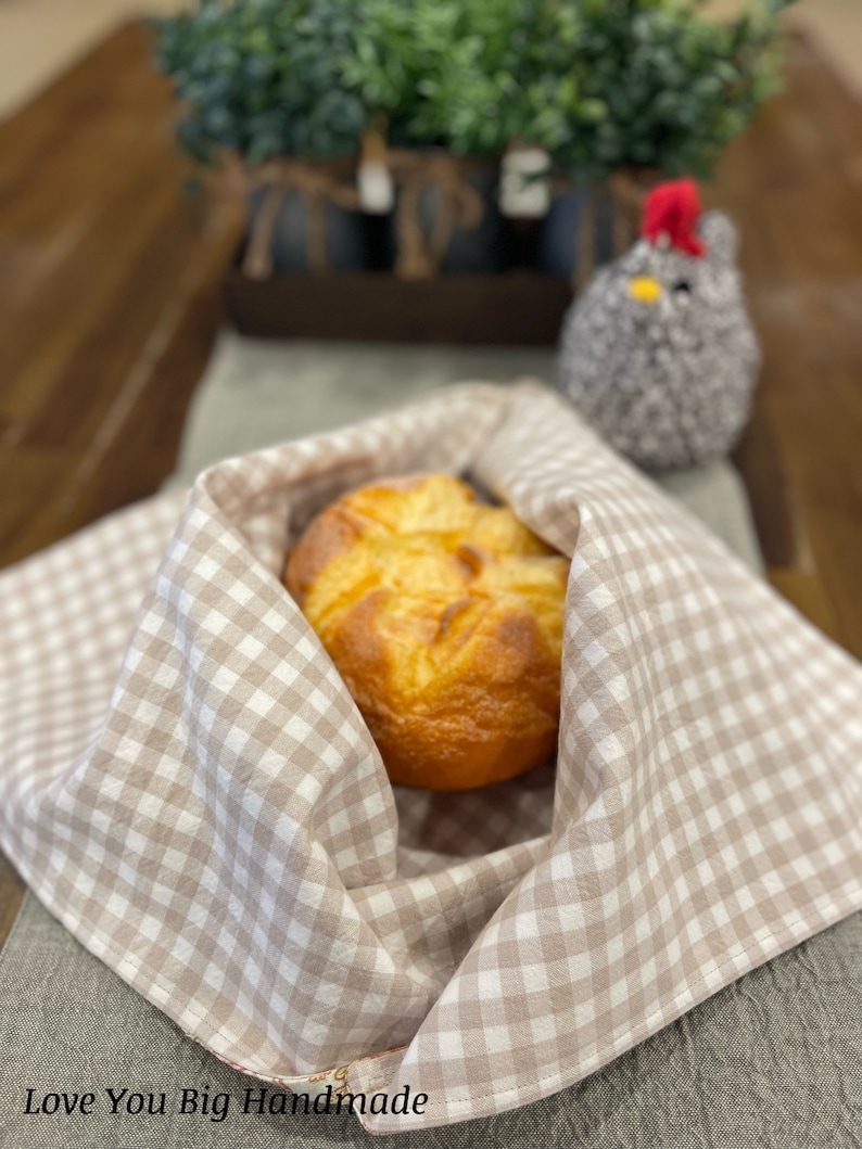 May include: A loaf of bread wrapped in a brown and white checkered cloth. The cloth has the words "Love You Big Handmade" printed on it.