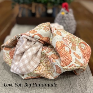 May include: A beige and brown fabric tote bag with a floral and basket pattern. The bag is folded and has a gingham lining. The text "Love You Big Handmade" is visible at the bottom of the image.