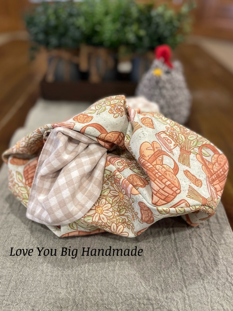 May include: A beige and brown fabric tote bag with a floral and basket pattern. The bag is folded and has a gingham lining. The text "Love You Big Handmade" is visible at the bottom of the image.