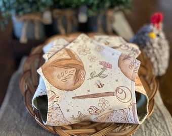 May include: A set of fabric coasters with a bread and floral pattern, resting in a woven basket. The coasters feature a beige background with brown and pink illustrations. The text "Love You Big Handmade" is visible at the bottom.