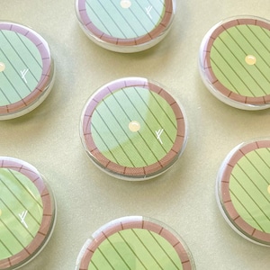 Pode incluir: Seis botões redondos verdes e marrons com um círculo branco no centro. Cada botão tem uma linha branca desenhada nele.
