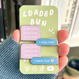 May include: A green and white pin with the text "LOADED BUN" and speech bubbles that say "your love" and "i miss that" and "i want that". The "i want that" bubble has a heart. Social media icons are at the bottom.