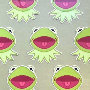 May include: Six green frog stickers with a pink open mouth and tongue. The frog stickers have a white outline and are on a light gray background.
