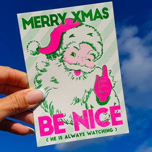 Carte de Noël imprimée Riso avec Père Noël rose fluo. Carte de joyeux Noël risographe aux couleurs néon et fabriquée à la main de manière écologique. Fabriqué avec une machine à riso.
