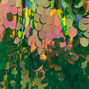 May include: Green iridescent sequins in a teardrop shape are sewn onto a sheer mesh fabric. The sequins are arranged in a scale-like pattern.