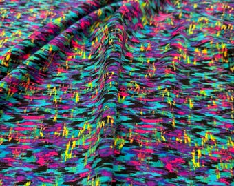 May include: A close-up of a colorful fabric with a black background. The fabric has a pattern of abstract shapes in shades of blue, green, pink, and yellow.