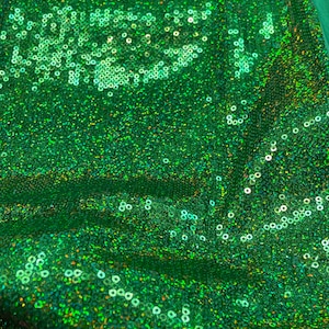 Pode incluir: Close-up de um tecido verde vibrante coberto de lantejoulas brilhantes. As lantejoulas são redondas e densamente compactadas, criando uma superfície texturizada. O tecido tem um leve brilho, refletindo a luz e adicionando profundidade à cor. O efeito geral é atraente e glamouroso.
