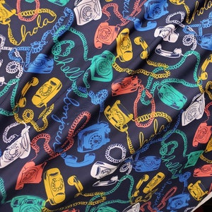 May include: A dark blue fabric with a repeating pattern of colorful rotary phones and coiled cords. The fabric has the word "Hola" written in a white cursive font.