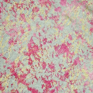 May include: A close-up of a fabric with a textured surface. The fabric is a light gray color with pink and gold accents.