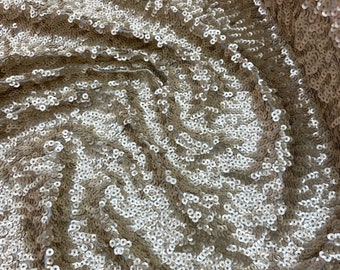May include: A close-up of a champagne-colored fabric with sequins. The sequins are arranged in a swirling pattern.