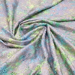 May include: A close-up of a silver fabric with a green and blue floral pattern. The fabric has a textured surface and a subtle shimmer.