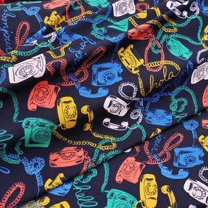 May include: A dark blue fabric with a repeating pattern of rotary phones and coiled cords. The phones are in various colors, including red, green, yellow, and white. The fabric has the words "Hola" and "Mama" printed on it.
