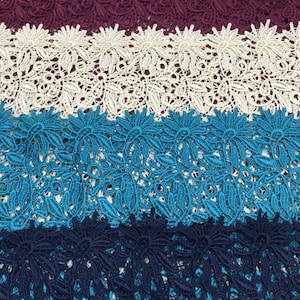 May include: Four strips of lace fabric in different colors. The top strip is burgundy, the second is white, the third is turquoise, and the bottom strip is navy blue. The lace has a floral pattern.