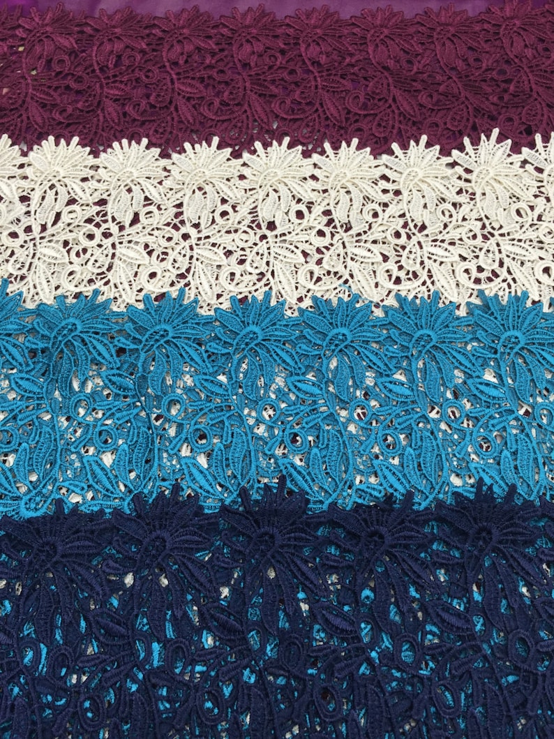 May include: Four strips of lace fabric in different colors. The top strip is burgundy, the second is white, the third is turquoise, and the bottom strip is navy blue. The lace has a floral pattern.