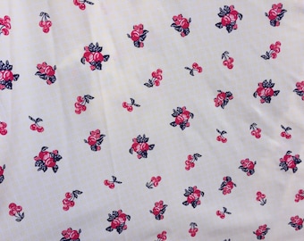 May include: A white fabric with a repeating pattern of red cherries and dark green leaves. The background is a light yellow with a subtle checkered pattern.