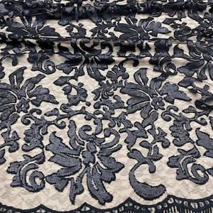 May include: Black sequined lace fabric with a floral pattern and a scalloped edge. The fabric has a fringe trim.