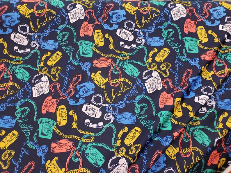May include: A dark blue fabric with a repeating pattern of vintage rotary phones, colorful phone cords, and the words "Hola", "Bonjour", and "Hello" in different languages.