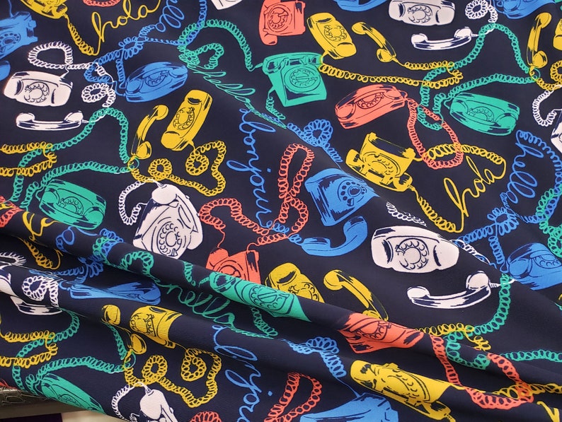 May include: A dark blue fabric with a repeating pattern of colorful rotary phones and the words "Hola", "Bonjour", and "Hello" in a variety of colors.