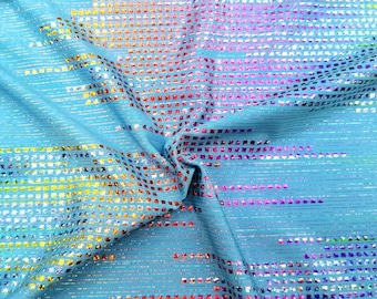 Op de afbeelding: Een lichtblauwe stof met een regenboogkleurig, iriserend patroon. De stof is bedekt met kleine, vierkante pailletten die een glinsterend effect creëren.