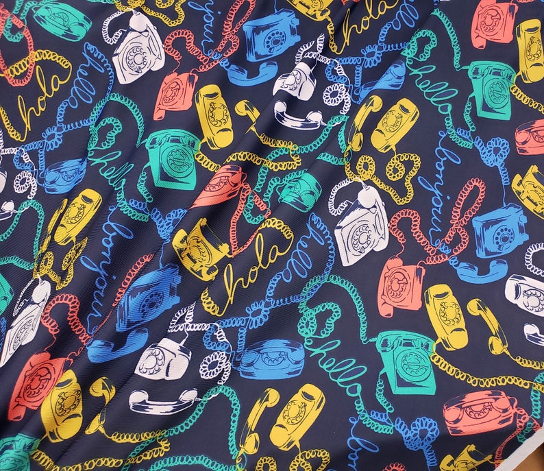 May include: A dark blue fabric with a repeating pattern of colorful rotary phones, phone cords, and the words "Hola", "Hello", and "Bonjour".