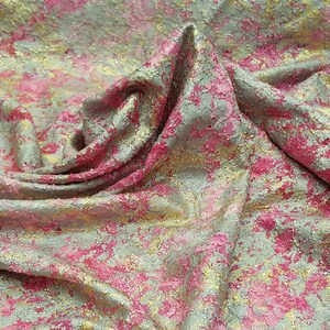 May include: Close-up of a pink and gold fabric with a textured, metallic finish. The fabric has a mottled appearance, with patches of pink and gold.