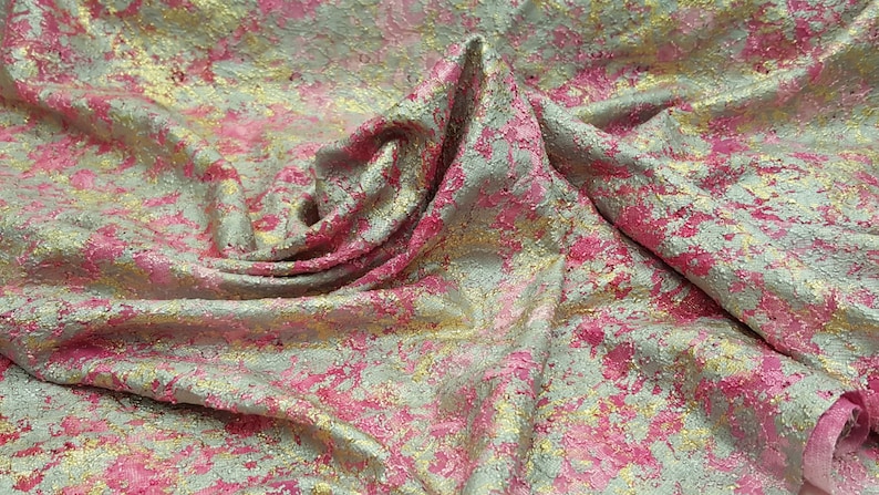 May include: Close-up of a pink and gold fabric with a textured, metallic finish. The fabric has a mottled appearance, with patches of pink and gold.