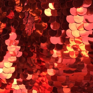 May include: Red sequin fabric with a shiny, iridescent finish. The sequins are arranged in a scale-like pattern.