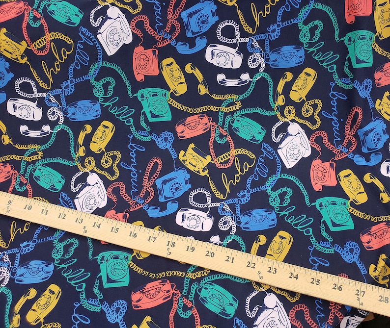 May include: A dark blue fabric with a repeating pattern of colorful rotary phones and the words "Hola", "Bonjour", and "Hello" in a white, yellow, and red font.