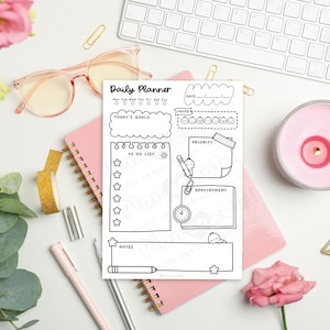 Puede incluir: Un planificador diario en blanco y negro con secciones para objetivos, listas de tareas y citas. El planificador est&aacute; sobre un cuaderno rosa, rodeado de art&iacute;culos de papeler&iacute;a, una vela y flores. El texto "Daily Planner" es visible.