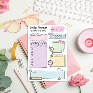 Puede incluir: Una composici&oacute;n plana con un planificador diario, un cuaderno rosa, gafas, un teclado y una vela encendida. El planificador incluye secciones para objetivos, listas de tareas y citas. Elementos florales y de papeler&iacute;a completan el arreglo.