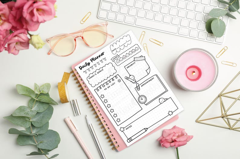 Puede incluir: Un planificador diario rosa con la frase "Daily Planner" en la parte superior. Incluye secciones para objetivos y citas. La imagen tambi&eacute;n muestra gafas rosas, un teclado, una vela y flores.