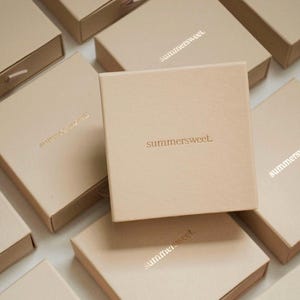 May include: A collection of beige square boxes with the word "summersweet" printed on the top. Some boxes are open, revealing a drawer. The boxes are arranged on a white surface.