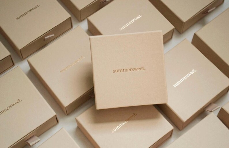 May include: A collection of beige square boxes with the word "summersweet" printed on the top. Some boxes are open, revealing a drawer. The boxes are arranged on a white surface.