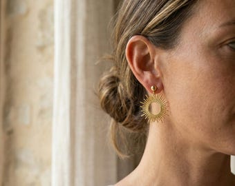 Peut inclure: Boucles d'oreilles dorées en forme d'éclat de soleil. Les boucles d'oreilles présentent un petit clou rond en haut, avec un motif d'éclat de soleil rayonnant vers l'extérieur. Le motif d'éclat de soleil a de multiples rayons pointus.