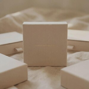 Puede incluir: Cuatro cajas rectangulares blanquecinas, una de pie, las otras planas. Las cajas est&aacute;n dispuestas sobre una superficie clara y texturizada. El texto "something sweet" est&aacute; en relieve en la parte delantera de la caja vertical. Dise&ntilde;o minimalista.