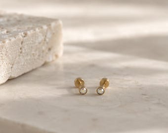 Può includere: Un paio di orecchini a lobo color oro con una singola gemma trasparente a taglio rotondo incastonata in una base di metallo. Gli orecchini presentano una chiusura piatta e circolare e una finitura lucida, con un design semplice e classico.