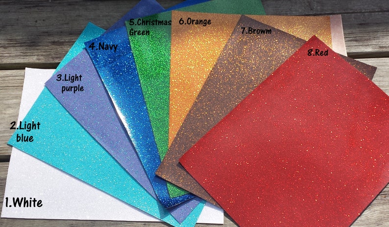 May include: A fan of glitter paper in various colors, including white, light blue, light purple, navy, Christmas green, orange, brown, and red. Each sheet is labeled with its color name.