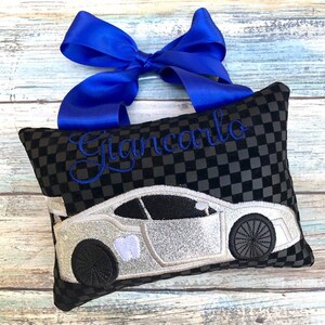 May include: A black and gray checkered pillow with a silver car design and the name "Giancarlo" embroidered in blue. A blue ribbon is tied at the top of the pillow.