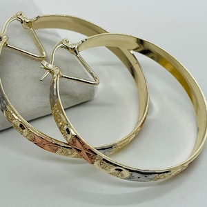 May include: A pair of gold hoop earrings with a decorative pattern featuring yellow, rose, and white gold accents. The earrings have a classic design with a secure clasp.