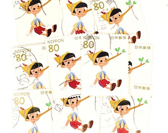 May include: A collection of nine vintage Japanese postage stamps featuring Pinocchio with a growing nose. Each stamp has the text "NIPPON" and "日本郵便" printed in black and gold. The stamps are in various conditions with some showing signs of wear and tear.