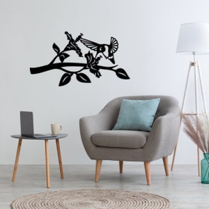 May include: Black metal wall art featuring a stylized bird perched on a branch with flowers. The art is displayed in a living room setting with a gray armchair and a side table.
